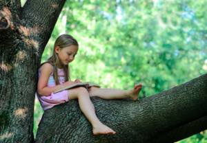 Little girl with a book on a tree branch